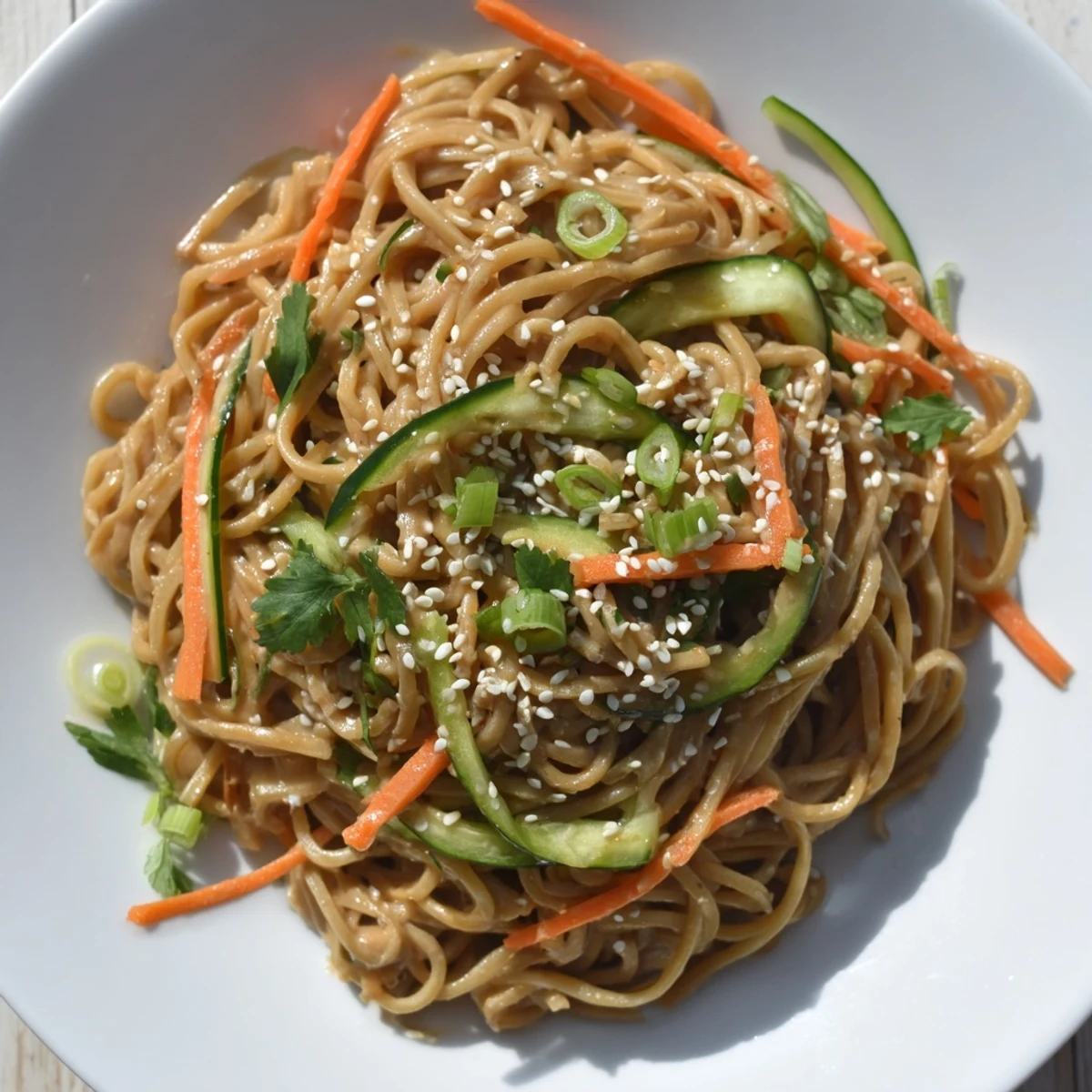 Slurpy cold sesame noodles, a delicious vegetarian meal, generously garnished with fresh herbs and peanuts.