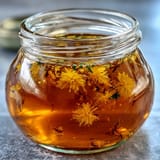 Dandelion jelly with fresh lemon and honey glows in a glass jar, its golden hue inviting a taste of spring.