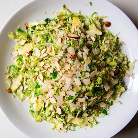 Vibrant Crunchy Lemon Parmesan Brussels Sprouts Salad topped with toasted almonds and fresh Parmesan cheese.