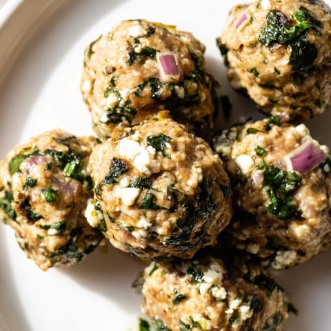 Close-up of juicy spinach feta turkey meatballs, ready to serve with a vibrant green herb garnish.