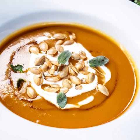 A steaming bowl of vibrant butternut squash soup, perfect for a cozy fall lunch or dinner.