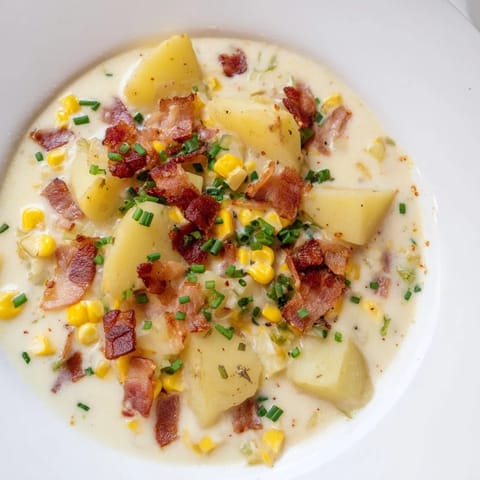 Close-up of creamy corn chowder soup with chunks of potato and smoky bacon crumbles piled on top.