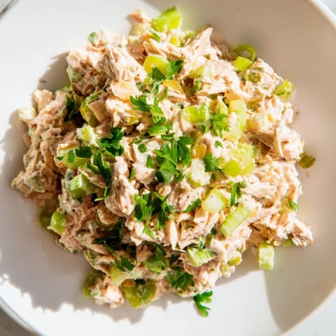Overhead view of Spicy Zesty Tuna Salad in a mixing bowl, featuring chopped scallions and creamy dressing.