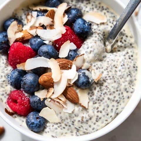 A close-up of poppy seed chia pudding with raspberries and shredded coconut, showing its thick, spoonable texture.  