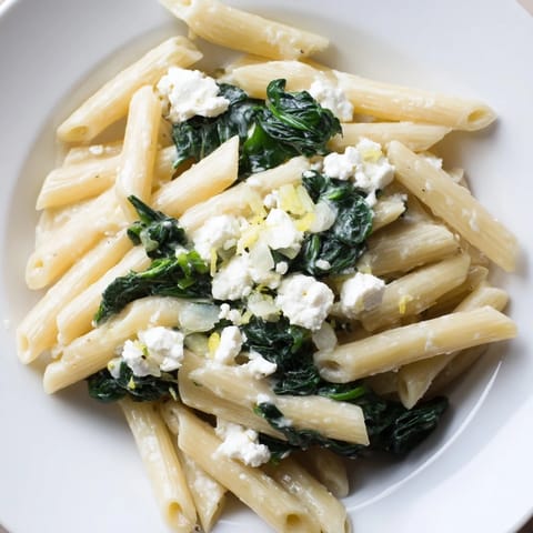 A close-up of Creamy Feta Spinach Pasta twirled on a fork, showing the velvety sauce clinging to penne.