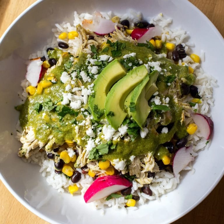 A close-up of a layered Green Enchiladas Rice Bowl, with melted cheese and a squeeze of lime.